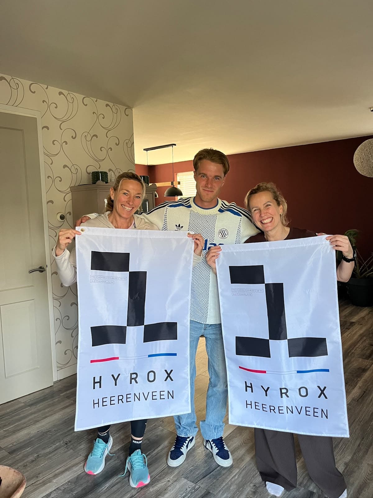 Teun met twee atleten die elk een podiumvlag van HYROX Heerenveen vasthouden.