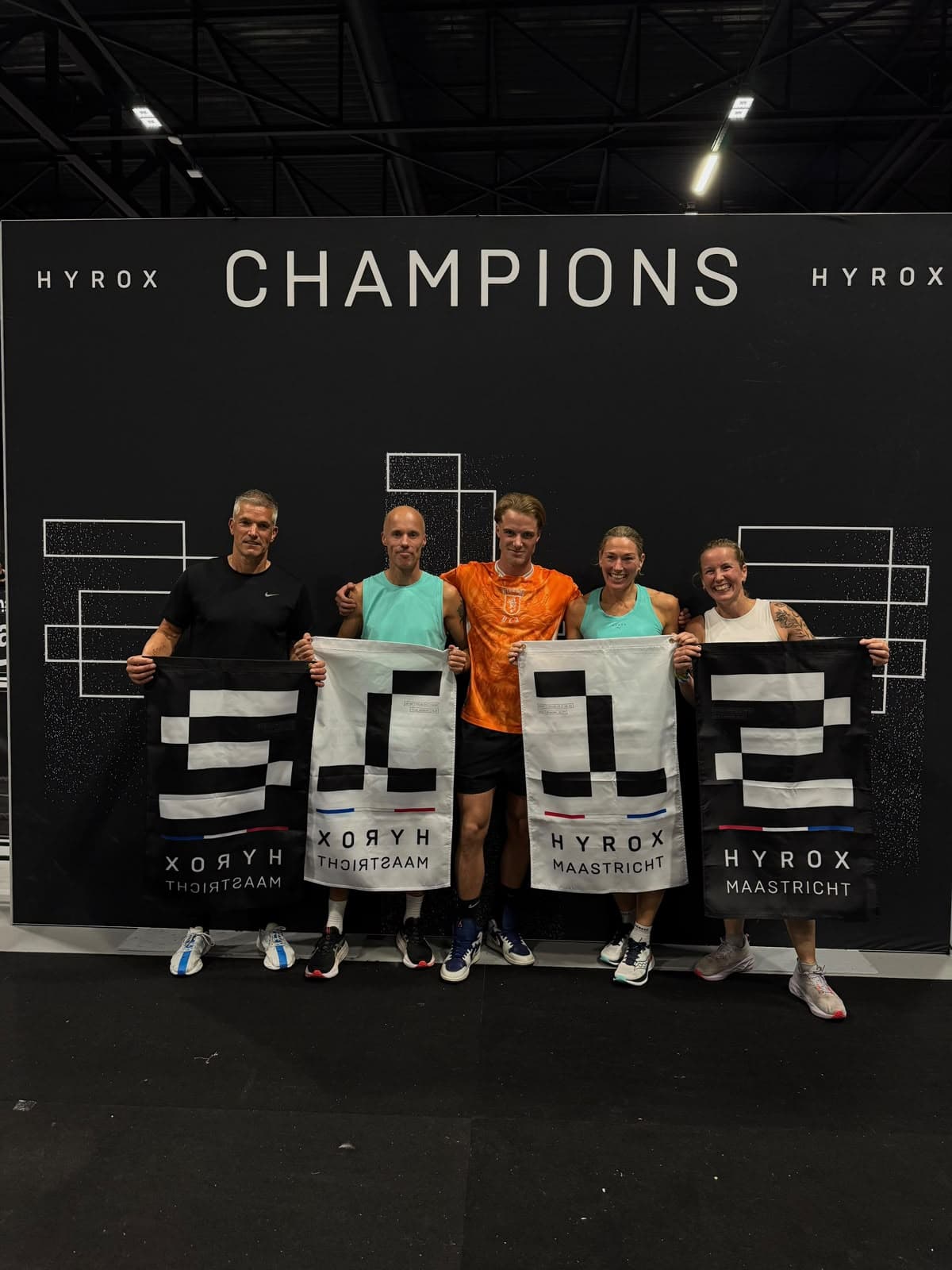 Teun met vier atleten die hun podiumvlaggen vasthouden voor de wand met Champions bij HYROX Maastricht.