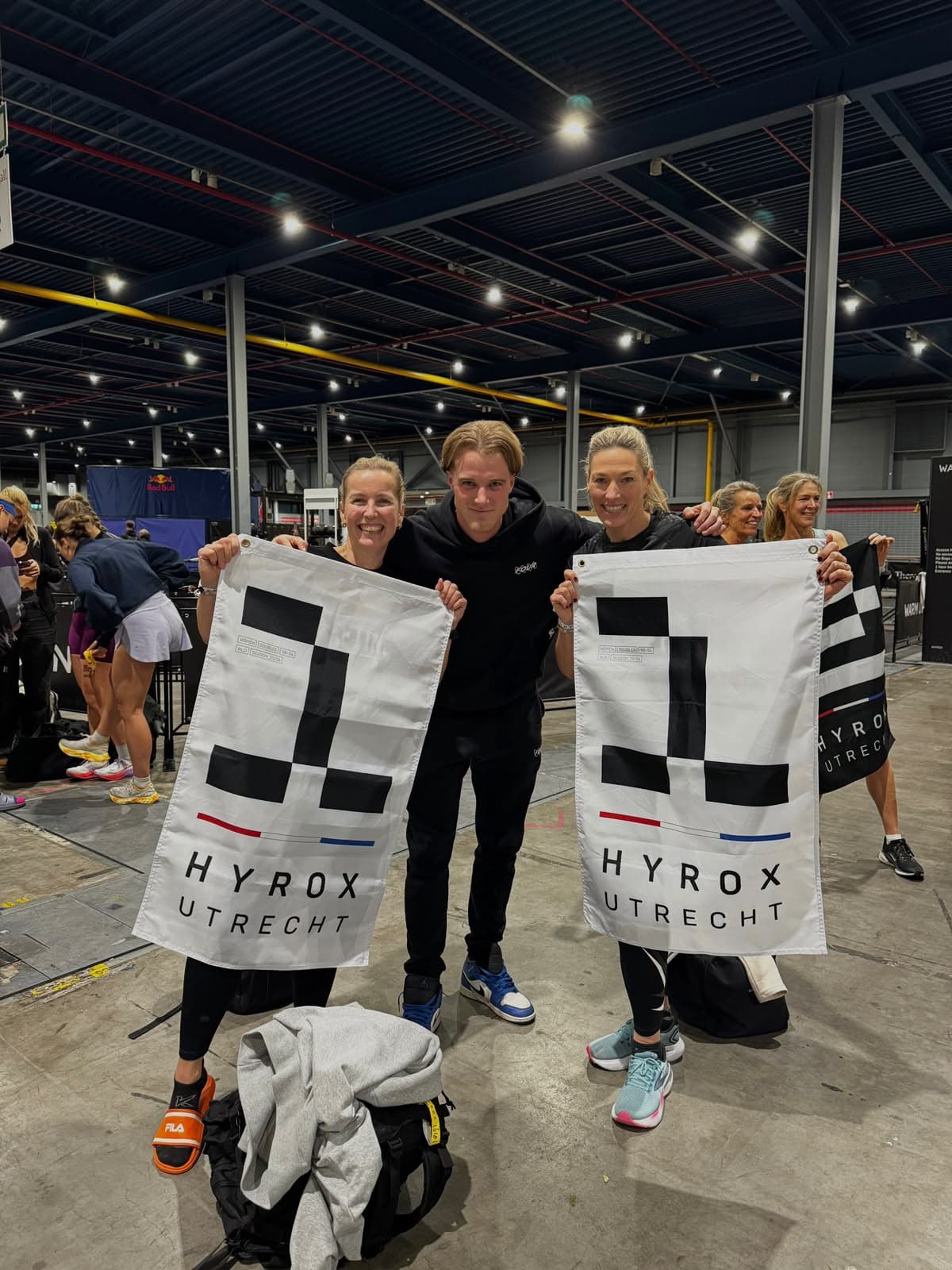 Teun tussen twee atleten die hun podiumvlaggen omhoog houden bij HYROX Utrecht.